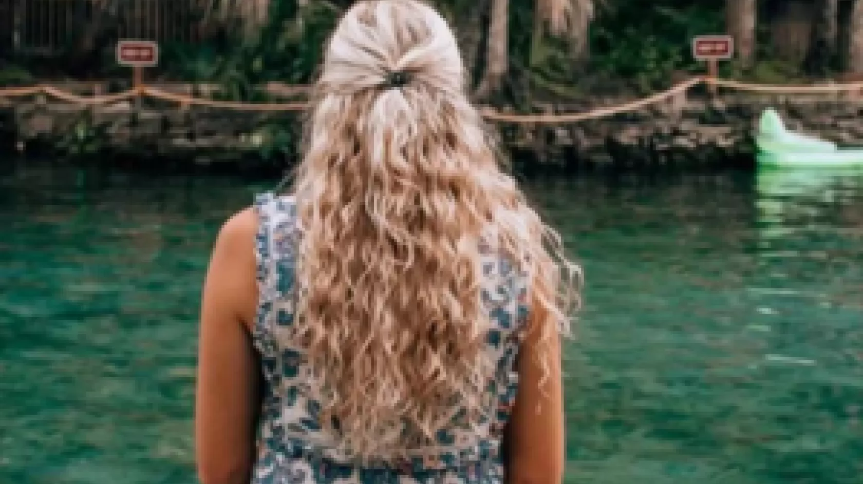 A woman sits near a clear body of water and looks out into the distance